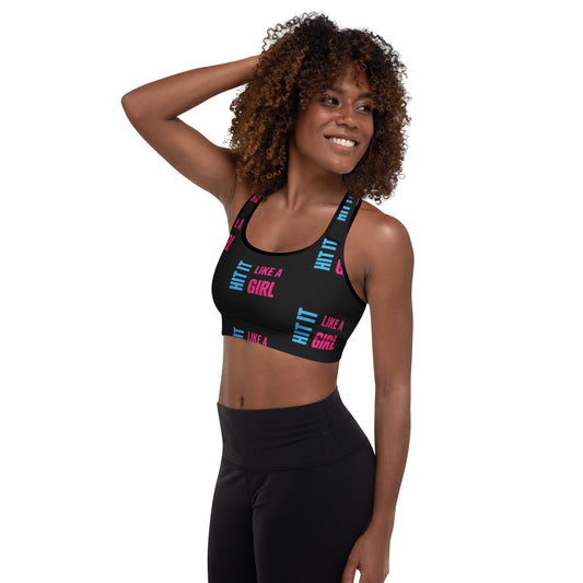 Smiling woman wearing a black "Hit It Like a Girl" sports bra with bold pink and blue text, styled for athletic wear or active lifestyle branding.