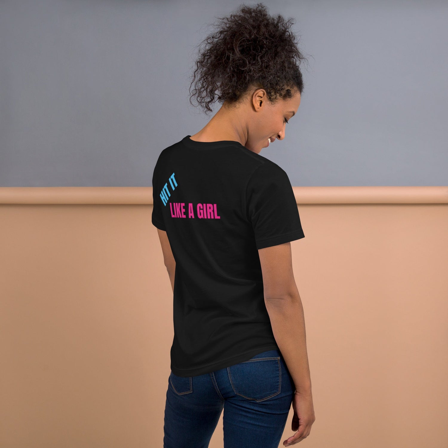 Woman wearing a black “Hit It Like a Girl” t-shirt in pink and blue text—empowering athletic tee designed for female volleyball players and active lifestyles.