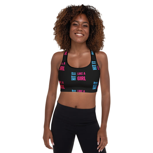Smiling woman wearing a black "Hit It Like a Girl" sports bra with bold pink and blue text, styled for athletic wear or active lifestyle branding.