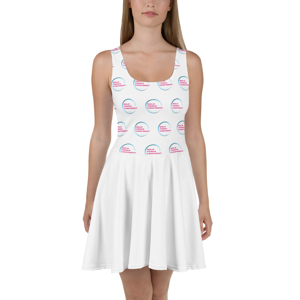 Woman wearing a white sleeveless skater dress patterned with the "Bold. Fierce. Confident." Hit It Like a Girl logo, combining sporty energy with feminine empowerment.