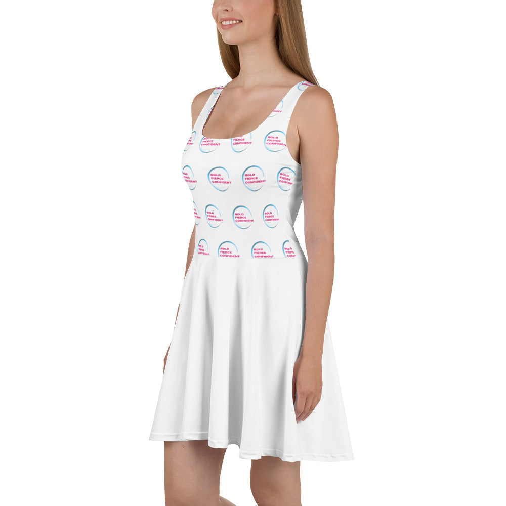 Woman wearing a white sleeveless skater dress patterned with the "Bold. Fierce. Confident." Hit It Like a Girl logo, combining sporty energy with feminine empowerment.