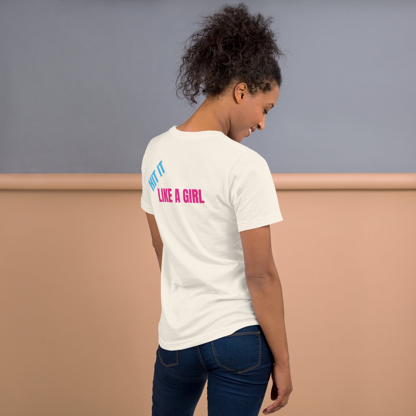 Woman wearing a vintage white "Hit It Like a Girl" athletic tee with bold blue and pink lettering on the back, standing confidently in casual jeans.